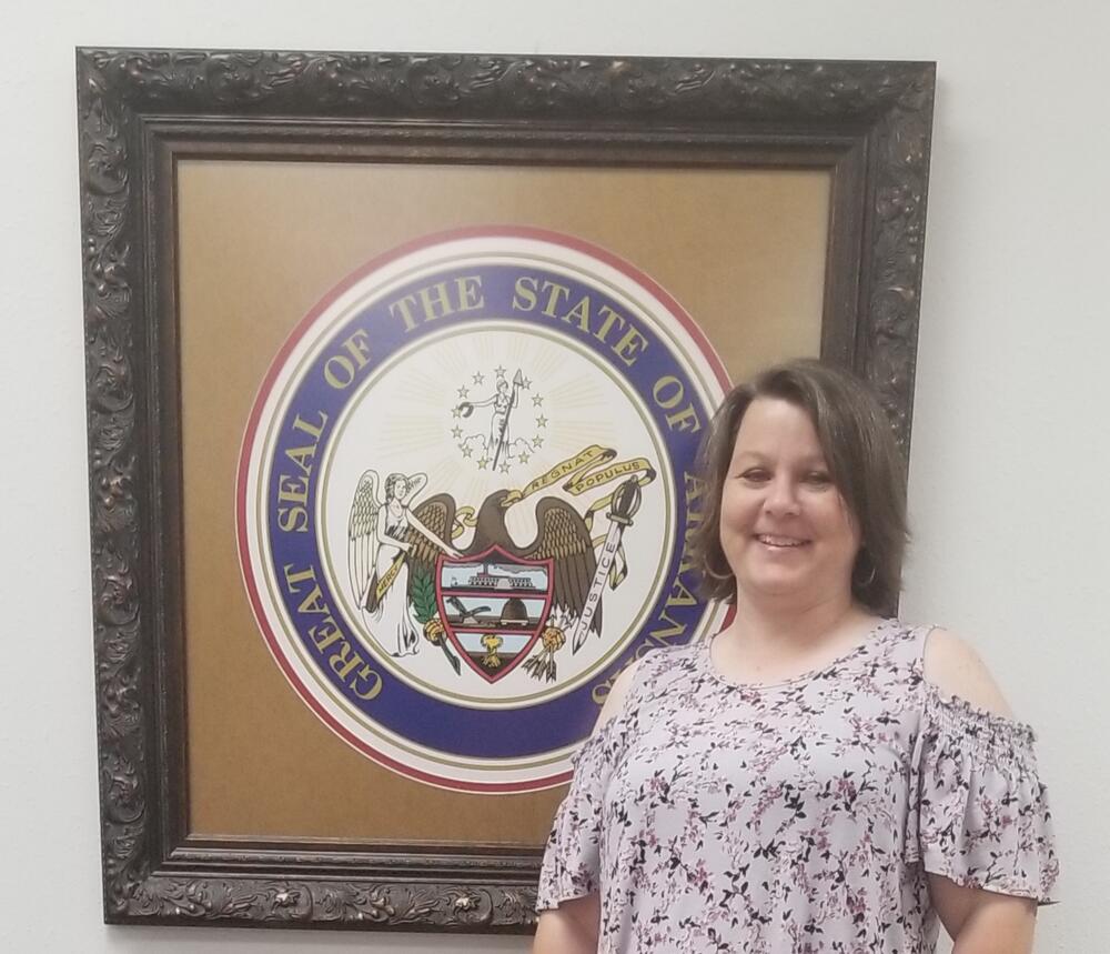 Kristie standing in front of Arkansas State Seal